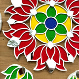 A colorful handcrafted rangoli design on a wooden surface, decorated with vibrant red, green, and yellow patterns, with additional small green and red shapes around it.