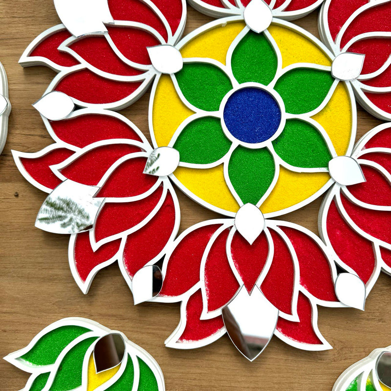 A colorful handcrafted rangoli design on a wooden surface, decorated with vibrant red, green, and yellow patterns, with additional small green and red shapes around it.